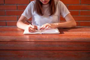 Aziatisch Dames slijtage wit overhemden schrijven beoordelingen en nemen aantekeningen met zonneschijn schijnend Aan handen. foto