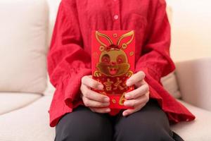 vrouw Holding Chinese rood envelop met gouden konijn en zegen woord, geld geschenk voor gelukkig maan- nieuw jaar vakantie. Chinese zin middelen geluk, gezond, Lucky en rijk foto