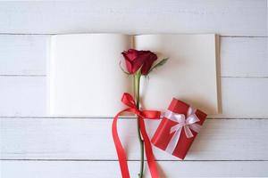 blanco notitieboekje met rood rozen en rood geschenk doos Aan houten tafel. kopiëren ruimte voor uw tekst. Valentijnsdag dag, bruiloft, verjaardag en speciaal gelegenheid concept. kopiëren ruimte voor tekst. top visie, vlak leggen. foto