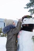 een kind verven een sneeuwpop gezicht met verven - winter vermaak en creativiteit, beeldhouwen een sneeuwman in winter buitenshuis. foto