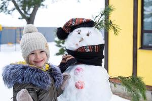 een kind verven een sneeuwpop gezicht met verven - winter vermaak en creativiteit, beeldhouwen een sneeuwman in winter buitenshuis. foto