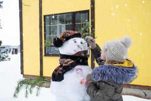 een kind verven een sneeuwpop gezicht met verven - winter vermaak en creativiteit, beeldhouwen een sneeuwman in winter buitenshuis. foto