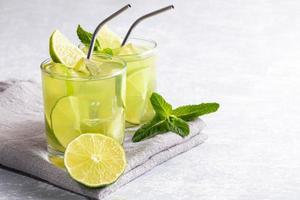 twee bril met bevroren groen matcha thee met limoen, ijs, vers munt en metaal drinken rietjes Aan licht grijs achtergrond. foto