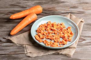 ronde turkoois bord met wortel chips Aan beige kleding stof en twee geheel wortels Aan houten tafel. foto