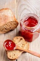 pot van aardbei jam, brood en houten lepel met jam Aan houten tafel. foto