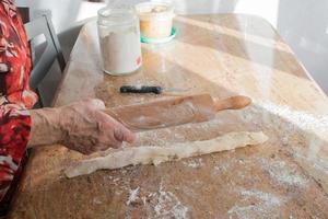 oud vrouw handen met een rollend pin voorbereidingen treffen de casadielles deeg Bij huis. tradicional gastronomie foto