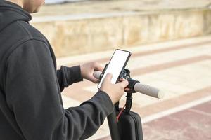 jong vrolijk Mens met e-scooter gebruik makend van scooter delen systeem toepassing Aan zijn smartphone foto