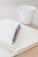 pen op een notitieboekje met een koffiekopje foto