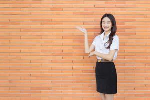 portret van een volwassen Thais leerling in Universiteit leerling uniform. Aziatisch mooi meisje staand naar Cadeau iets vol vertrouwen Aan steen muren achtergrond. foto