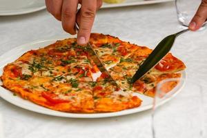 plat leggen. detailopname van mensen handen nemen plakjes van peperoni pizza van houten bord. tafel geserveerd met zwart textiel servet. smartphone Aan tafel. mensen eten snel voedsel in cafe. foto