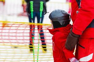 weinig meisje in rood aan het leren naar ski met de helpen van een volwassen foto