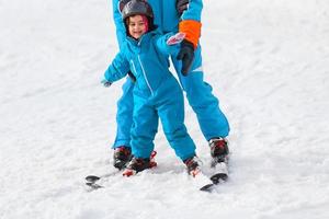 weinig meisje leert naar ski met de helpen van een volwassen foto