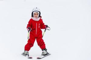 weinig meisje in rood pak is skiën naar beneden een berg foto