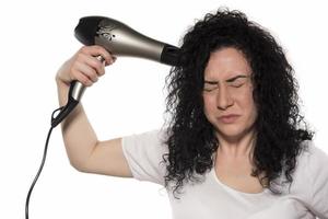 mooi meisje gebruik makend van een haar- droger en lachend. natuurlijk jong vrouw drogen gekruld haar- met droog haar machine. foto