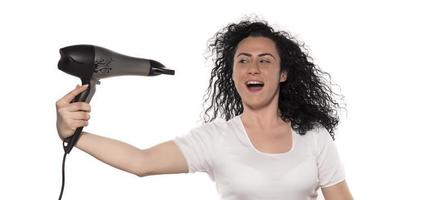 mooi meisje gebruik makend van een haar- droger en lachend. natuurlijk jong vrouw drogen gekruld haar- met droog haar machine. foto