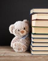 teddy beer gluren uit van achter een stack van boeken, zwart achtergrond foto