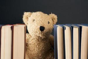 teddy beer gluren uit van achter een stack van boeken, zwart achtergrond, terug naar school- foto
