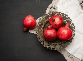 rijp rood granaatappels liggen in een ronde metaal kom Aan een zwart tafel foto