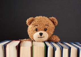 teddy beer gluren uit van achter een stack van boeken, zwart achtergrond foto