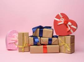 stack van cadeaus verpakt in bruin kraft papier en gebonden met zijde lint, dozen Aan een roze achtergrond foto