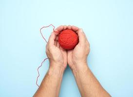 twee mannetje handen houden een bal van rood wollen draden, blauw achtergrond foto