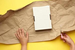 rechthoekig wit karton doos en twee vrouw handen zijn verpakt met bruin papier Aan een geel achtergrond foto