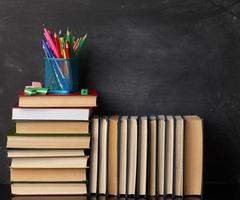 stack van divers boeken, schrijfbehoeften Aan zwart krijt bord achtergrond, terug naar school- foto