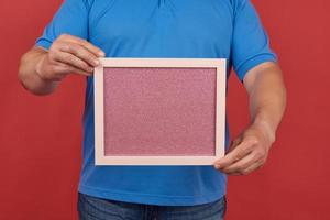 Mens in een blauw t-shirt houdt een leeg rechthoekig roze kader voor schrijven tekst foto