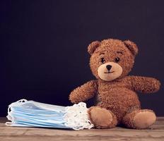 bruin teddy beer zittend en beschikbaar medisch masker Aan een zwart schoolbord achtergrond foto