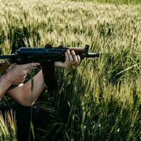 een soldaat met een militaire aanvalsgeweren ak 74 staat in een veld, Oekraïense tarwevelden en oorlog. foto