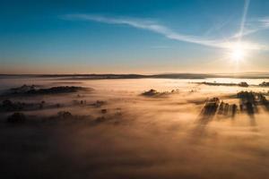 vliegend over- een dorp Bij ochtendgloren, helder zon Aan de horizon en mist over- een klein dorp. foto