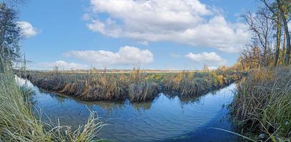 panoramisch beeld van natuurlijk stroom in voorkant van groot weide Oppervlakte in zonneschijn foto