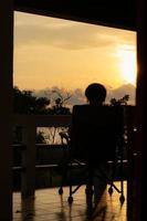 silhouet Dames persoon kom tot rust alleen Aan een stoel en genieten tropisch natuur in de ochtend- met koffie tijd, vakantie vakantie, leven vrijheid concept. foto