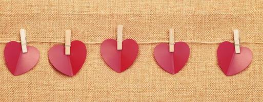 rood harten Aan kleren pin Aan bruin textiel achtergrond foto
