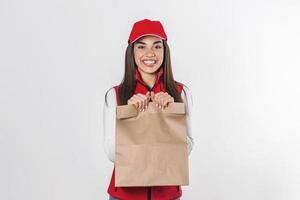 levering vrouw werknemer in rood pet t-shirt uniform masker handschoen houden ambacht papier pakket met voedsel geïsoleerd Aan wit achtergrond foto