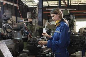 een industrieel arbeider in beschermend en veiligheid uniform en harde hoed, jong Kaukasisch vrouw ingenieur werken met metaalwerk machine in fabricage fabriek. professioneel productie mechanisch bezigheid. foto