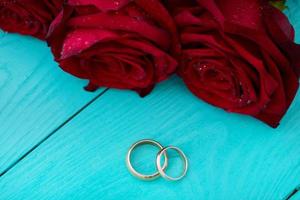 bruiloft ringen en rood rozen. bruiloft boeket Aan blauw houten achtergrond. selectief focus. kopiëren ruimte foto