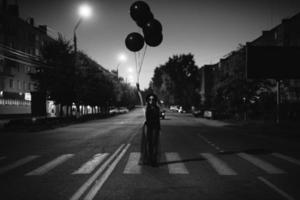 een meisje in zwart met zwart ballonnen in haar handen poses staand Aan de weg foto