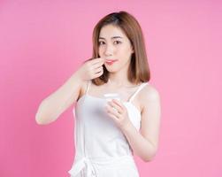 beeld van jong Aziatisch vrouw aan het eten yoghurt Aan roze achtergrond foto