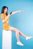 vol lengte foto van jong Aziatisch vrouw gebruik makend van smartphone Aan blauw achtergrond