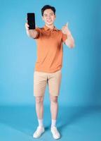 beeld van jong Aziatisch Mens Holding smartphone Aan blauw achtergrond foto