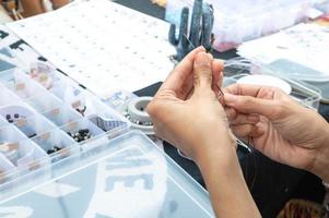 detailopname van een vrouw handen rijgen kralen Aan de draad, maken sieraden in de werkplaats. foto