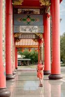 verticaal afbeelding. een Aziatisch vrouw vervelend traditioneel cheongsam qipao jurk Holding ventilator en glimlach terwijl bezoekende de Chinese boeddhistisch tempel. Chinese nieuw jaar concept foto