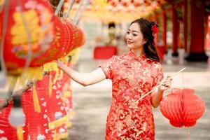 gelukkig Chinese nieuw jaar. Aziatisch vrouw vervelend traditioneel cheongsam qipao jurk op zoek zelfverzekerd Holding en spelen lantaarn terwijl bezoekende de Chinese boeddhistisch tempel. emotie glimlach foto