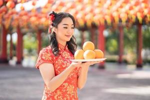 gelukkig Chinese nieuw jaar. mooi Aziatisch vrouw vervelend traditioneel cheongsam qipao jurk Holding vers sinaasappels in Chinese boeddhistisch tempel. bidden voor het beste wens zegen en mooi zo geluk foto