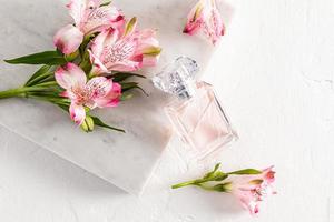 een fles van parfum of toilet water met een bloemen licht geur leunde Aan een marmeren wit plaat met roze bloemen. wit achtergrond. aroma presentatie. foto