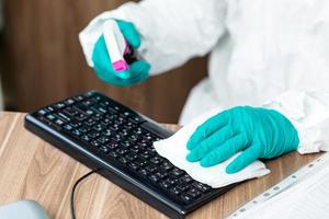 persoon in beschermend pak die een computertoetsenbord met spray schoonmaakt foto