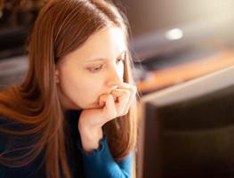 jong meisje leunend haar gezicht Aan haar hand- en op zoek Bij computer toezicht houden op werken of aan het studeren online Bij huis. zacht focus. foto