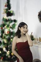 portret van een mooi jong meisje vervelend een rood gewaad, glimlachen Bij de camera, staand in versierd Kerstmis leven kamer binnenshuis foto
