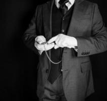 portret van butler in donker pak en wit handschoenen richten naar tijd Aan zak- horloge. concept van onderhoud industrie en professioneel efficiëntie. foto